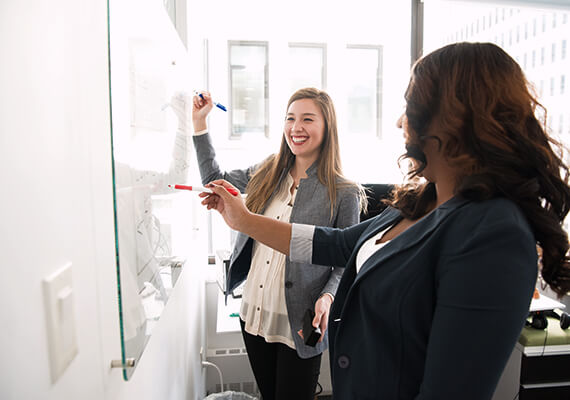 A professor and smiling teacher both write on whiteboard